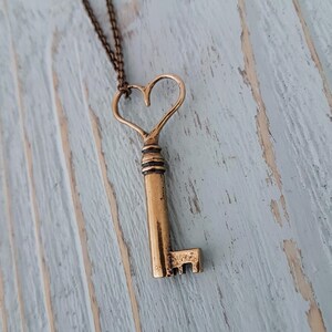 Op de afbeelding: Een gouden ketting met een sleutel in de vorm van een hart. De sleutel hangt aan een ketting en aan een houten oppervlak.