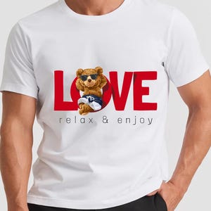 May include: White t-shirt featuring a red "LOVE" graphic and a cartoon bear wearing sunglasses, shorts, and trainers. The text "relax & enjoy" is printed below the word "LOVE".