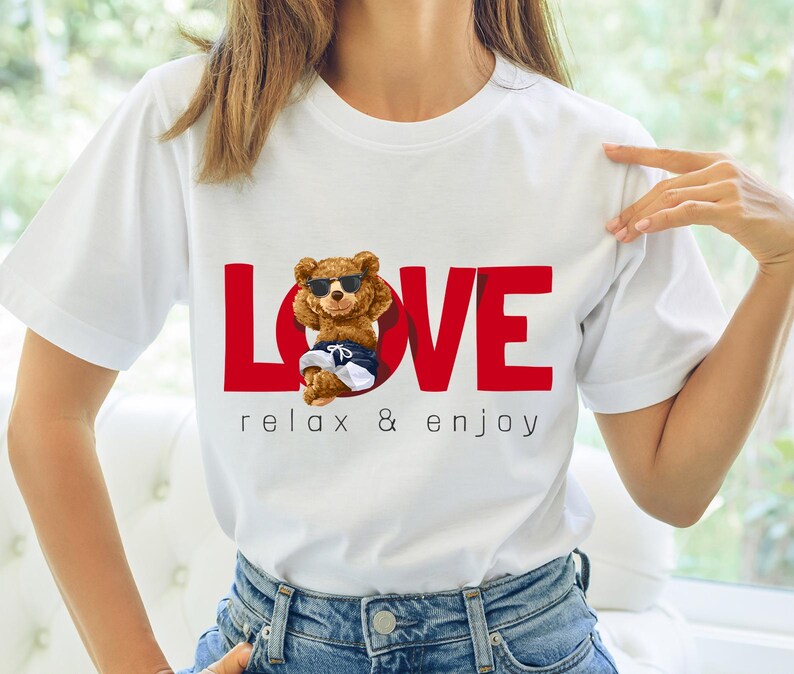 May include: White t-shirt featuring a red "LOVE" graphic and a cartoon bear wearing sunglasses and swim trunks. The text "relax & enjoy" is below the graphic. The shirt is made of a soft material and is suitable for casual wear.