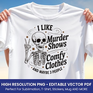 Puede incluir: Camiseta blanca con un gráfico negro y dorado que presenta un esqueleto haciendo el signo de la paz. El texto dice "I LIKE Murder Shows Comfy Clothes AND MAYBE 3 PEOPLE". La camiseta se muestra sobre un fondo de cielo azul.