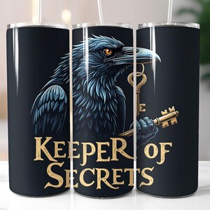 May include: A black tumbler featuring a detailed illustration of a raven holding a golden key. The raven has blue and black feathers and orange eyes. The text "KEEPER OF SECRETS" is in gold lettering.