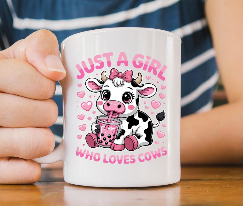 May include: White ceramic mug with a cartoon cow design. The cow, with a pink bow, is drinking a pink drink. The mug has the text "JUST A GIRL WHO LOVES COWS" in pink. The cow has black and white spots and is surrounded by pink hearts.