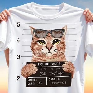 May include: White t-shirt featuring a cat wearing sunglasses, designed as a police mugshot. The cat holds a sign that reads "Sofa Destroyer." The shirt includes a mugshot background with numbers and text: "POLICE DEPT.", "CRIME: 1/2", and "CODE: # 180326781."