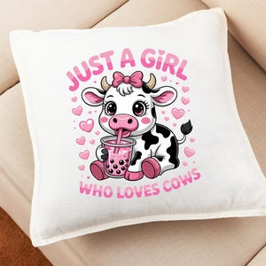 May include: Square white cushion featuring a cartoon cow design. The cow is black and white with a pink bow, drinking from a pink drink. The text reads "JUST A GIRL WHO LOVES COWS" in pink.