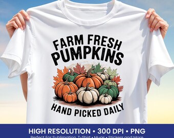 Może przedstawiać: Biała koszulka z ilustracją dyni w odcieniach pomarańczu, zieleni i bieli, z jesiennymi liśćmi. Tekst "FARM FRESH PUMPKINS HAND PICKED DAILY" jest wydrukowany nad i pod dyniami.