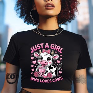 May include: Black crop top with the text "JUST A GIRL WHO LOVES COWS" in pink. The graphic features a cartoon cow with a pink bow, drinking a pink beverage, surrounded by pink hearts.