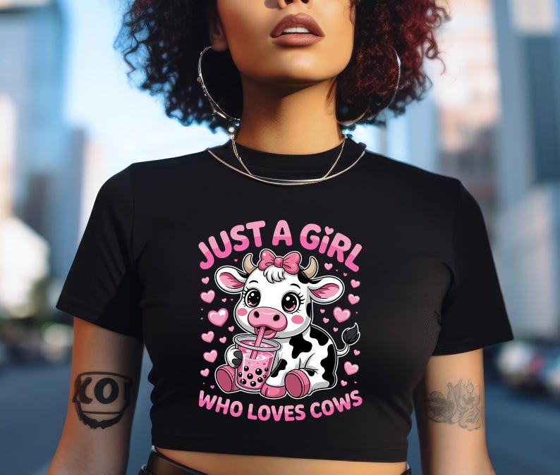 May include: Black crop top with the text "JUST A GIRL WHO LOVES COWS" in pink. The graphic features a cartoon cow with a pink bow, drinking a pink beverage, surrounded by pink hearts.