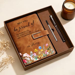 May include: A brown notebook with a metal clasp, a pen, and a refill in a gift box. The cover features a floral print and the text: MAY YOU be proud of THE WORK YOU DO THE PERSON YOU ARE AND THE DIFFERENCE YOU MAKE FOR Avery.