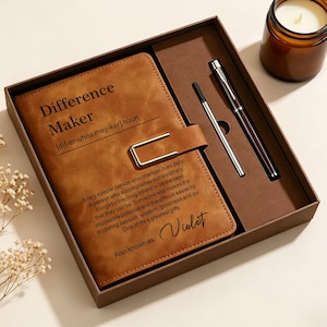 May include: A brown leather-like notebook with a metal clasp, featuring the text Difference Maker and a definition, alongside a pen and a refill in a brown gift box. The notebook cover is personalized with the name Violet at the bottom.