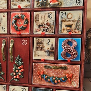 Puede incluir: Un calendario de adviento de madera con m&uacute;ltiples cajones que presentan ilustraciones navide&ntilde;as, incluyendo ratones, Santa Claus y paisajes invernales. Cada caj&oacute;n est&aacute; numerado y algunos muestran elementos decorativos en relieve como coronas y bayas.