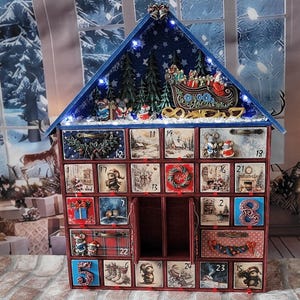 Puede incluir: Un calendario de Adviento de madera con forma de casa y veinticuatro cajones numerados. El techo presenta un fondo azul estrellado, pinos en miniatura y un trineo de Santa. Cada caj&oacute;n muestra ilustraciones festivas, incluyendo ratones, regalos y escenas navide&ntilde;as, con algunos cajones que presentan detalles decorativos tridimensionales.