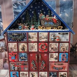 Puede incluir: Un calendario de adviento de madera con forma de casa y veinticuatro cajones numerados. El techo presenta un trineo en miniatura, a Santa Claus y pinos. Cada caj&oacute;n muestra ilustraciones navide&ntilde;as, relieves decorativos y tiradores met&aacute;licos.