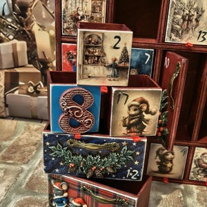 Puede incluir: Un calendario de adviento de madera con m&uacute;ltiples cajones que presentan varias ilustraciones con motivos navide&ntilde;os, incluyendo ratones, Santa Claus y escenas invernales. Los cajones est&aacute;n numerados y algunos tienen tiradores decorativos.