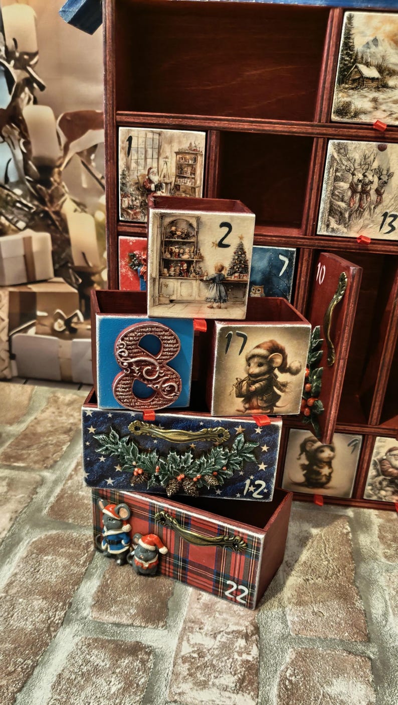 Puede incluir: Un calendario de adviento de madera con m&uacute;ltiples cajones que presentan varias ilustraciones con motivos navide&ntilde;os, incluyendo ratones, Santa Claus y escenas invernales. Los cajones est&aacute;n numerados y algunos tienen tiradores decorativos.