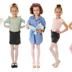 May include: Five young girls in various outfits stand against a white background. They wear tops, skirts, shorts, and tights with polka dots. One girl holds a book, and another holds a stuffed animal. The girls wear shoes and headbands.