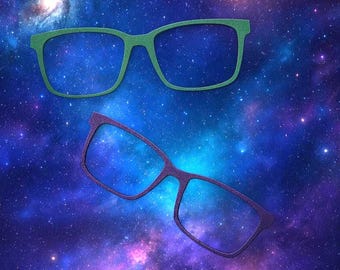 May include: Two pairs of spectacle frames, one in a solid green colour and one in a solid purple colour, both featuring a rectangular shape with a textured surface finish, positioned against a vibrant, colourful nebula background with stars.