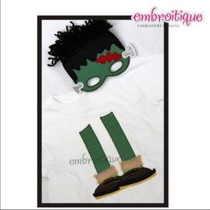 May include: A white t-shirt with green and brown embroidered legs and shoes. A green and black Frankenstein mask with a red scar is on top of the shirt.