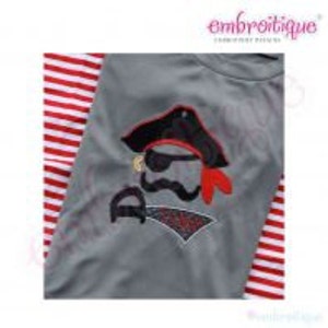May include: Gray t-shirt with an embroidered pirate design featuring a black hat, an eye patch, a red bandana, a mustache, and a sword. The pirate's name is "Aiden".