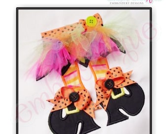 May include: Embroidered witch boot design with orange and black polka dots, a yellow bow, and a black button. The design is on a white fabric background.