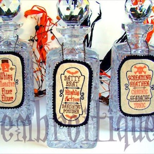 May include: Three clear glass bottles with decorative labels. The labels are printed with Halloween-themed text and images. The bottles are filled with a clear liquid. The text on the labels reads: "Whiny Monster Fixer Elixer", "Batty Brat Highly Active Banishing Powder", and "Screaming Heathen Chronic Headache Tonic".