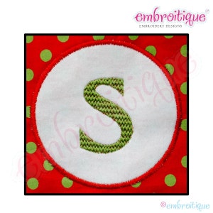 May include: A white circle with a green embroidered letter "S" on a red background with green polka dots.