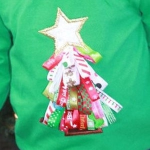 Peut inclure: Un t-shirt vert à manches longues avec une étoile blanche et une décoration en ruban coloré ressemblant à un sapin de Noël.