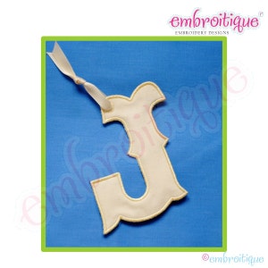 May include: A cream-colored felt letter J with a decorative edge, hanging from a white ribbon against a blue background. The letter is a simple, classic design, perfect for adding a personalized touch to a craft project.