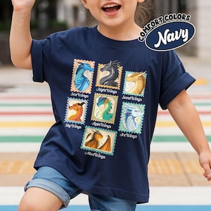 May include: Navy blue t-shirt featuring colorful dragon illustrations resembling postage stamps. Each stamp showcases a different dragon type with names like SeaWings, NightWings, and SandWings. The shirt has the text "COMFORT COLORS Navy".
