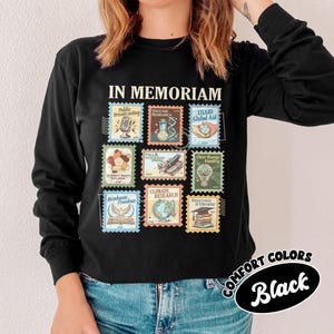 May include: Black long-sleeve shirt with a stamp design. The stamps feature various themes, including "Public Broadcasting," "Vaccine Research," and "Climate Research." The shirt also has the words "IN MEMORIAM" and "COMFORT COLORS Black."