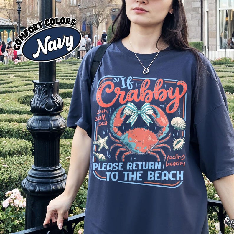 May include: Navy blue t-shirt with a crab graphic and the text "If Crabby, Please Return to the Beach." The design includes a crab, seashells, and starfish. The shirt is a Comfort Colors brand.