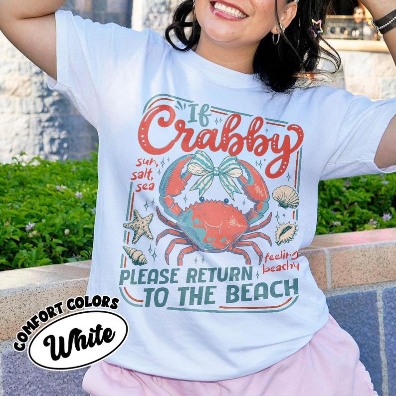 May include: White t-shirt with a colorful graphic featuring a crab, seashells, and the text "If Crabby, Please Return to the Beach." The design includes the words "sun, salt, sea" and "feeling beachy."