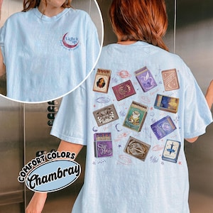 May include: Light blue Comfort Colors Chambray t-shirt with a small crescent moon and text graphic on the front. The back features various matchbox designs with illustrations and text, including stars and planets.