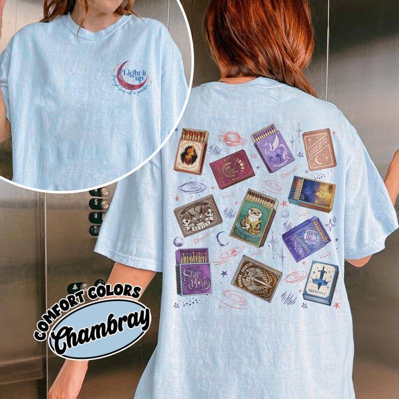 May include: Light blue Comfort Colors Chambray t-shirt with a small crescent moon and text graphic on the front. The back features various matchbox designs with illustrations and text, including stars and planets.