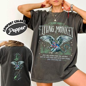 May include: Dark gray t-shirt with a graphic of a winged creature and the text "FLYING MONKEY". The shirt also features the text "Just one cackle from the wicked and we will come and carry you away your little dog too."