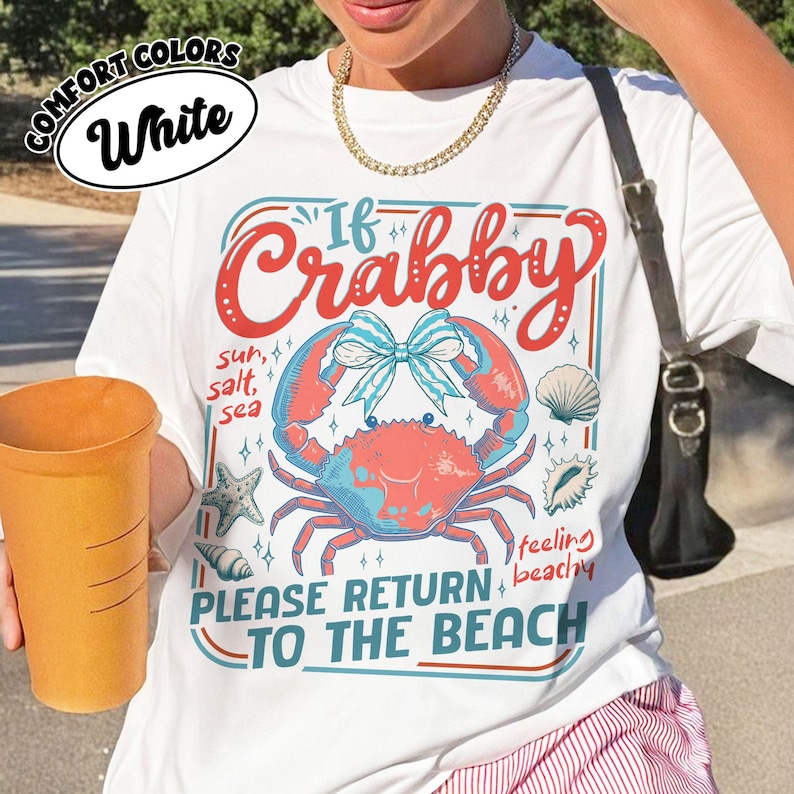 May include: White t-shirt with a crab graphic and the text "If Crabby, Please Return to the Beach." The design includes a crab, seashells, and starfish in red, blue, and white. The shirt is made of Comfort Colors material.