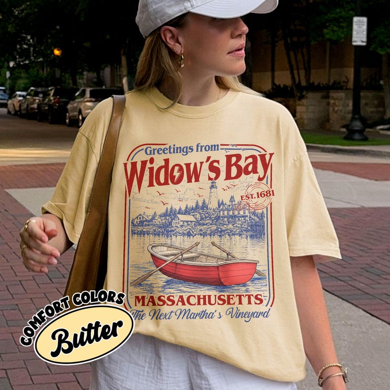 May include: A butter yellow short-sleeve t-shirt featuring a graphic print with the text Greetings from Widow's Bay, EST. 1681, Massachusetts, The Next Martha's Vineyard. The design includes a red rowboat, a lighthouse, and coastal scenery.