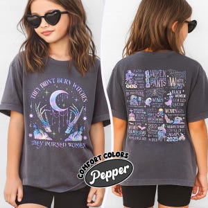 May include: Dark gray t-shirt with the text "THEY DIDN'T BURN WITCHES, THEY BURNED WOMEN." The front features a crescent moon and skeleton hands. The back has a list of women's rights milestones. The shirt is from Comfort Colors.