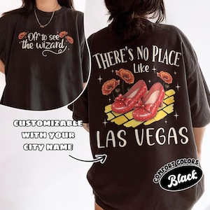 May include: Black t-shirt with the text "Off to see the wizard" on the front and "There's no place like Las Vegas" on the back. The back design features red shoes, poppies, and a yellow brick road.