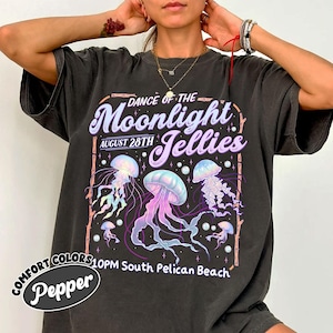 May include: Dark gray t-shirt with a graphic design featuring jellyfish in shades of pink, purple, and blue. The text reads "Dance of the Moonlight Jellies, August 28th, 10PM South Pelican Beach". The shirt has a vintage, worn look.