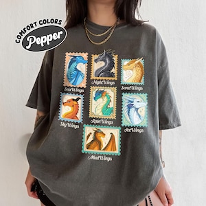 May include: Dark grey t-shirt featuring a collection of dragon illustrations in postage stamp designs. The stamps showcase various dragon types with names like SeaWings, NightWings, and SandWings. The shirt has the text "COMFORT COLORS Pepper".