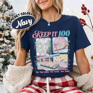 May include: Navy blue t-shirt with the text "KEEP IT 100" and three illustrated panels. The panels depict a geometric structure, a monorail with a geodesic sphere, and a boat with ducks. The shirt also has the text "On The Land. The Seas. The Skies."