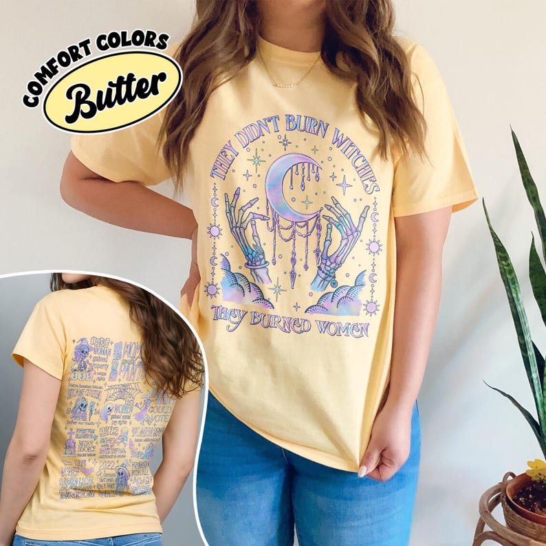 May include: Butter-colored t-shirt with the text "THEY DIDN'T BURN WITCHES THEY BURNED WOMEN" and a graphic of skeletal hands holding a crescent moon. The back of the shirt features a list of words and images.
