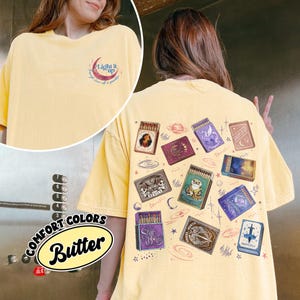 May include: Butter yellow Comfort Colors t-shirt with a graphic of matchboxes on the back. The matchboxes have various illustrations, including a mermaid, a unicorn, and a cat. The front of the shirt has the text "Light it up" and the Comfort Colors logo.