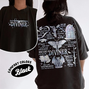 May include: A black t-shirt featuring a graphic print. The front displays a sword and the word DIVINER. The back features a large design with a moth, a gargoyle, a sword, a gothic window, a book, and text including DIVINER and various quotes.