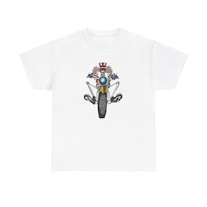 May include: White t-shirt featuring a motorcycle design with patriotic elements. The graphic includes a motorcycle with a skull wearing a hat, American flags, and stars. The motorcycle has a yellow frame and black tires.