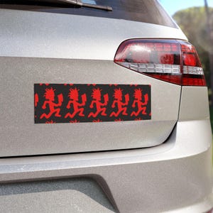 May include: A rectangular bumper sticker applied to the silver trunk of a vehicle. The sticker features a repeating pattern of a red running figure holding a cleaver against a solid black background, creating a bold and high-contrast graphic design.
