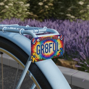 Könnte beinhalten: Fahrradkennzeichen mit dem Wort "GR8FUL" auf einem Batik-Hintergrund, mit tanzenden Bären und Rosen. Das Schild ist an einem hellblauen Fahrrad befestigt. Die Worte "Grateful Dead" stehen oben.