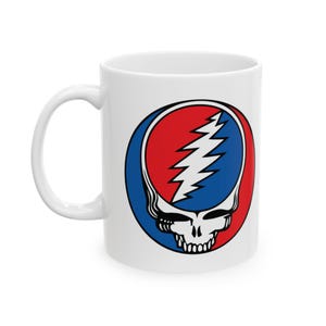 May include: White ceramic mug featuring the iconic Steal Your Face logo. The design includes a skull with a lightning bolt, set within a red and blue circle. The mug has a curved handle for easy gripping.