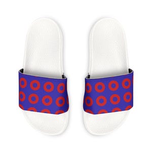 May include: A pair of white slide sandals with a blue strap featuring a pattern of red circles. The sandals have a textured footbed and a black interior lining.