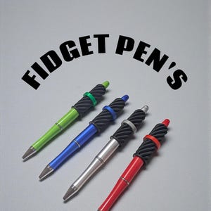 May include: Four colorful fidget pens with black textured grips and silver tips are displayed against a gray background. The pens are green, blue, silver, and red, each with a coordinating colored ring. The text "FIDGET PEN'S" is arched above the pens.